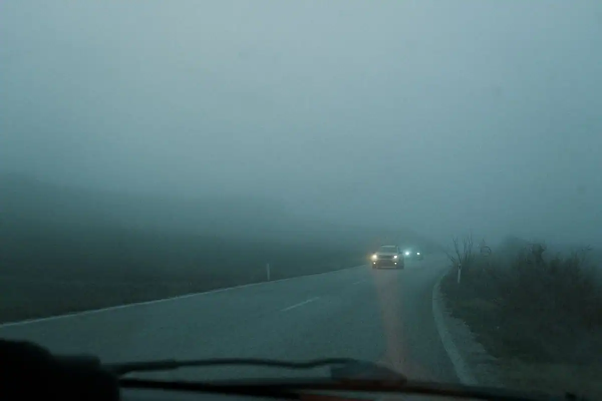 Parbrizul unei mașini în ceață densă, cu o lumină slabă pe șosea