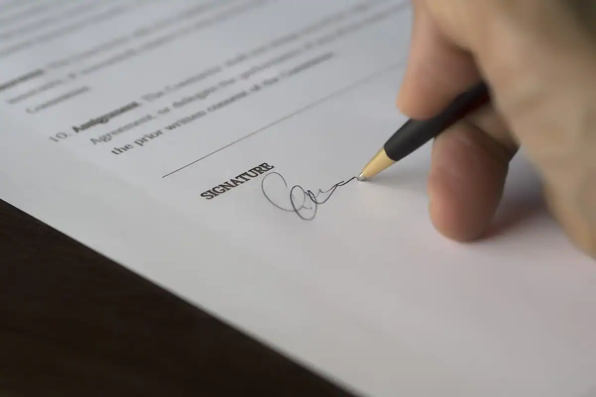 Mână care semnează cu creionul un contract, în dreptul rubricii pentru semnătură