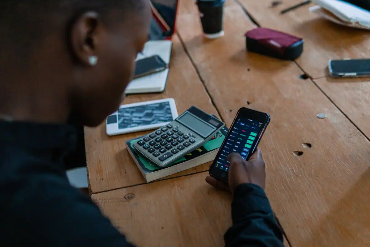 Persoană care face calcule pe telefon, cu un calculator lângă ea pe masă