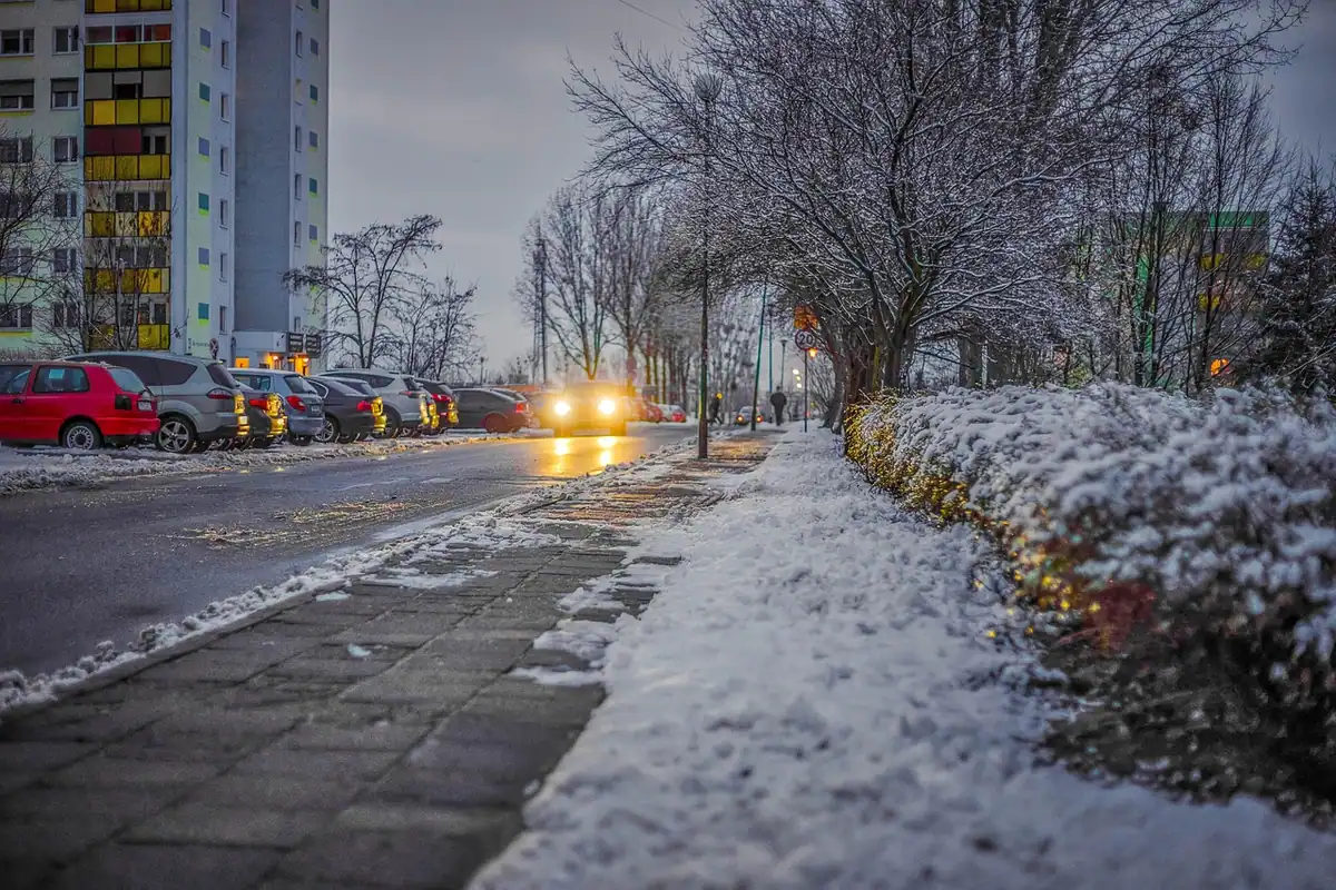 Stradă cu zăpadă la lăsarea serii, cu o mașină cu farurile aprinse, în condiții de iarnă