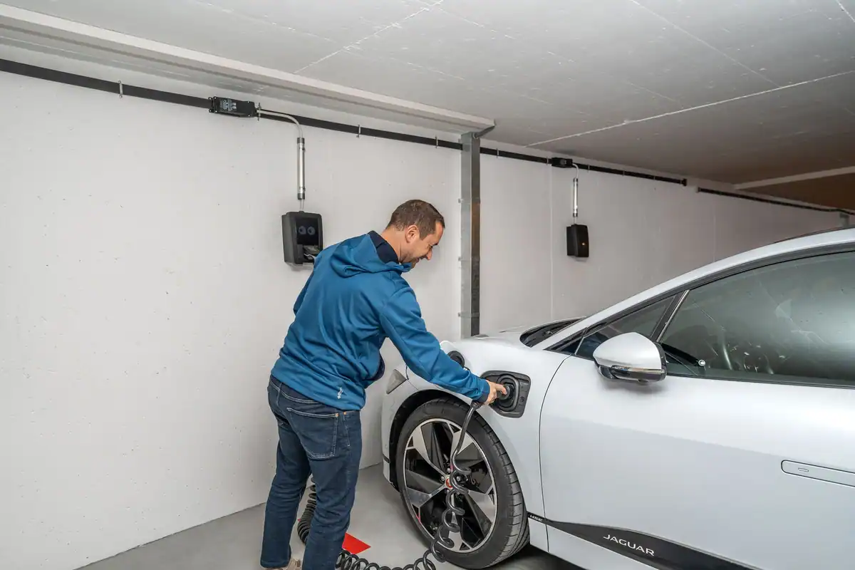 Bărbat care conectează o mașină electrică la stația de încărcare din garaj