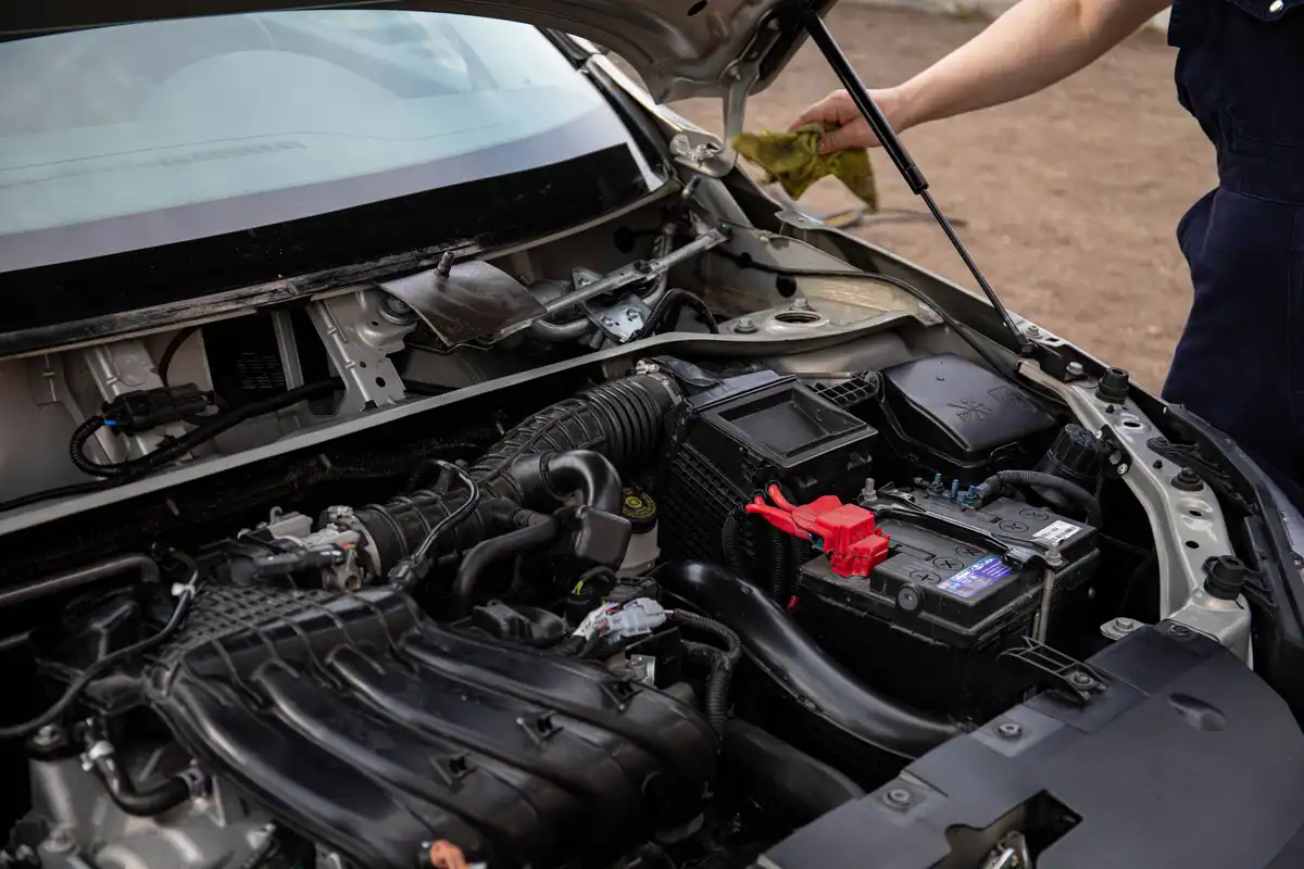 Mecanic care inspectează compartimentul motor și bateria în timpul unei revizii de rutină