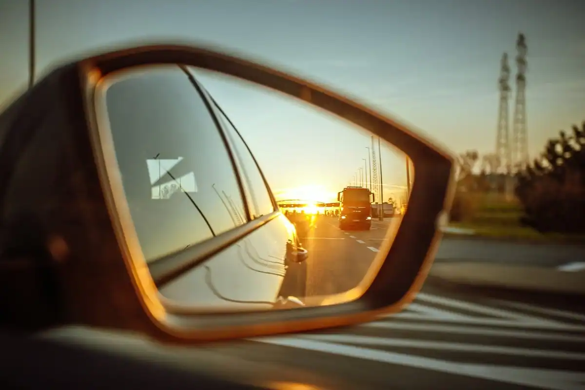Oglinda laterală a unei mașini cu un apus reflectat și drumul din spate