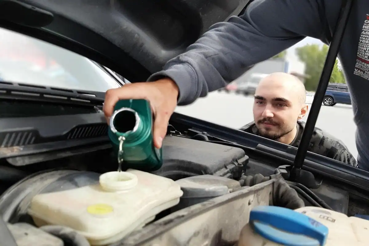 Bărbat care toarnă lichid dintr-un bidon în motorul unei mașini cu capota ridicată