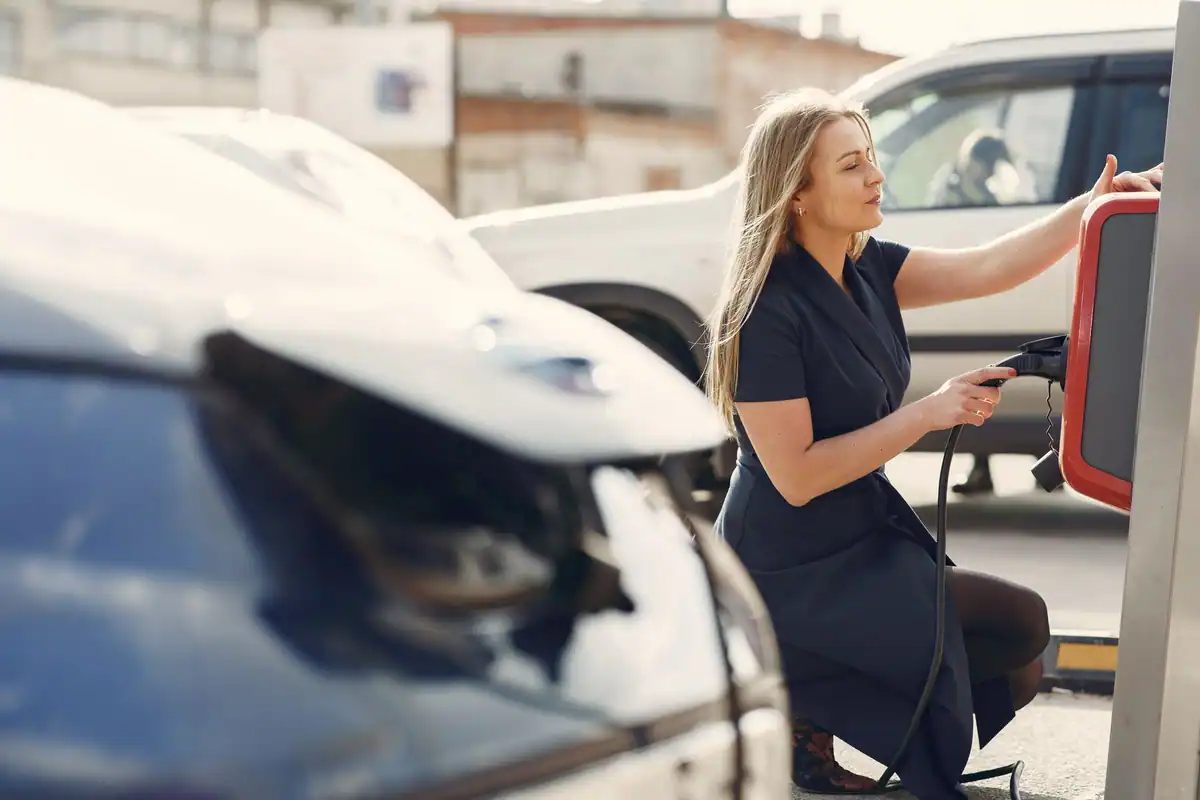 Femeie care conectează o mașină electrică la o stație de pe stradă