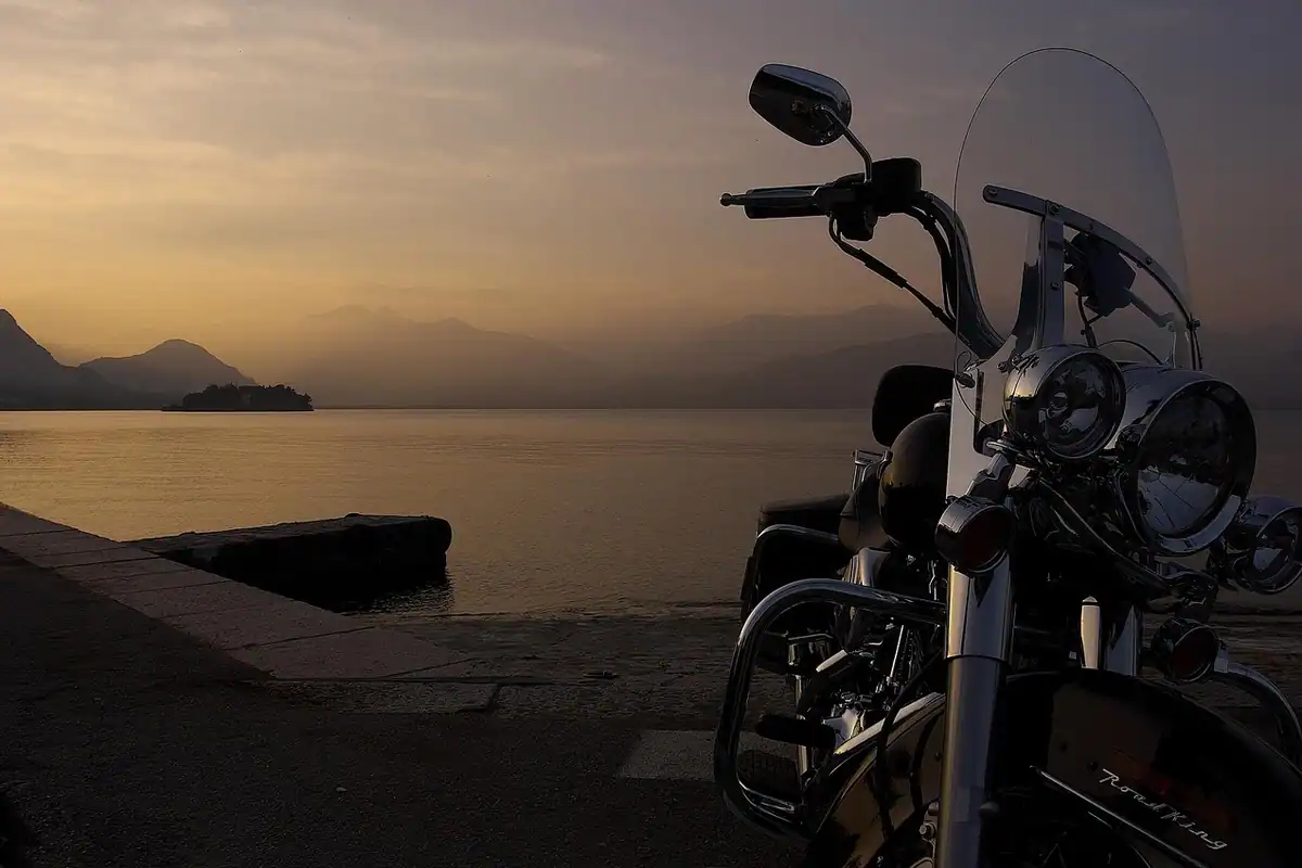 Motocicletă Harley-Davidson pe un drum lângă un lac, la apus, imagine de drum cu parbriz ce cere lichid curat